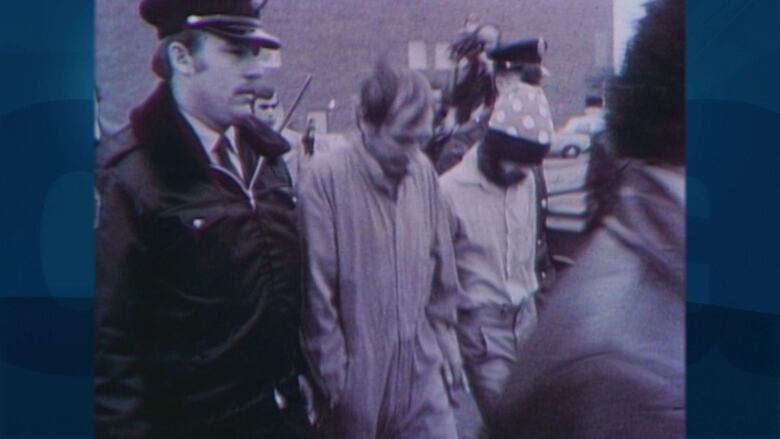 Black and white film photo of two men being walking next to police