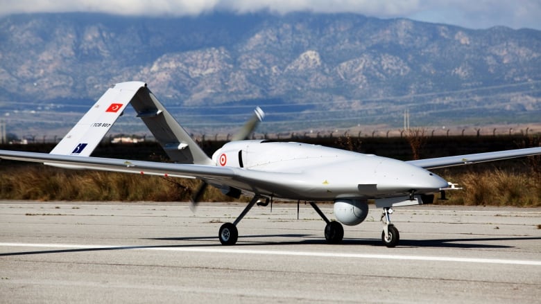 A large white drone is photographed on a runway. It has the Turkish flag on one of its rudders at the back.