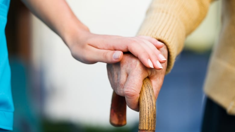 Young person holding the hand of an older person, who is holding a cane.