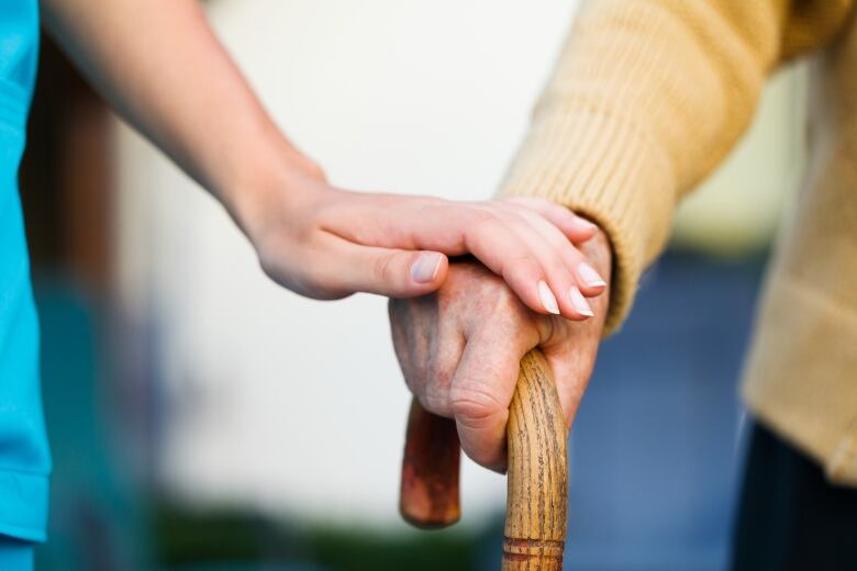 Young person holding the hand of an older person, who is holding a cane.