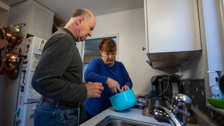 A woman stirs a pot over a kitchen counter while an older man studies what she's doing.