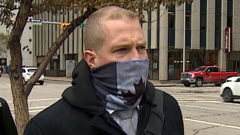 A man walks down the street wearing a black and white mask with the Canadian flag on it. 