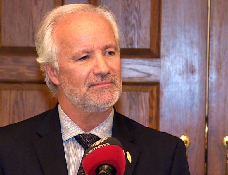 Older man with beard in black suit against wooden door.