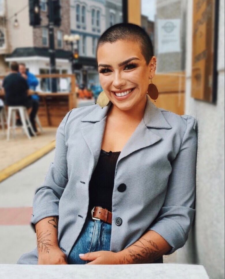 A woman with a buzz cut smiles at the camera. She is wearing a blazer and dangly earrings. 