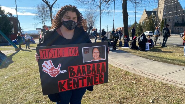 A woman stands outside holding a poster.