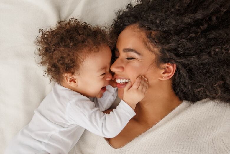 A woman and baby play together on a bed. 