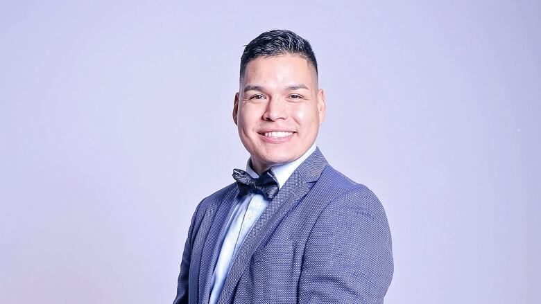 A man in a suit jacket, shirt and bowtie smiles at the camera.