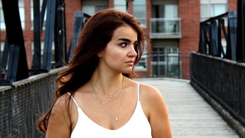 young Arab woman with red hair in white tank top standing on a bridge looking into the distance.