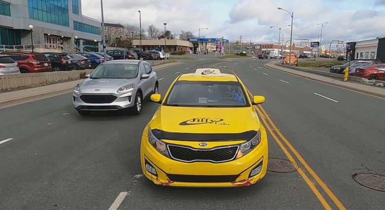 A yellow taxi cab and a grey SUV drive side-by-side on a road.