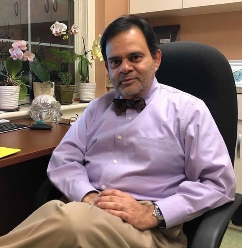 A man sits in a chair wearing a purple dress shirt and bowtie.