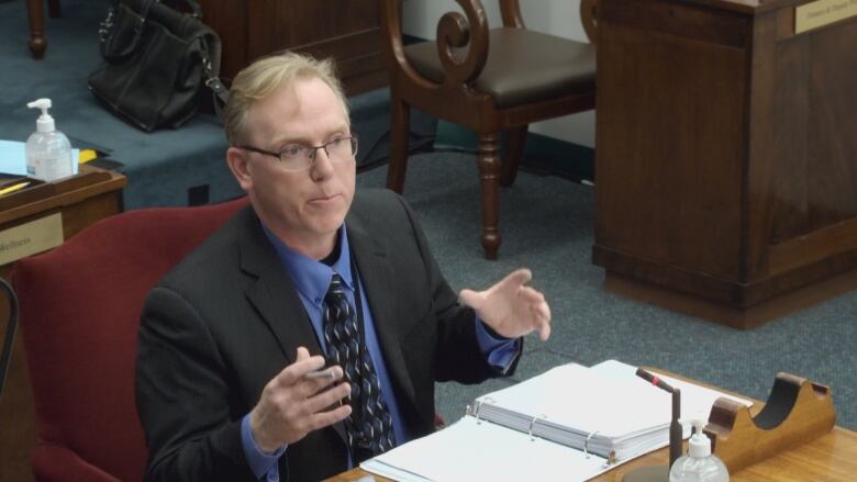 Man with glasses in business suit sits at a desk in the Prince Edward Island legislative chamber. 