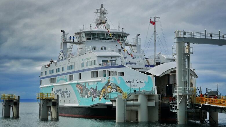 A ferry with an elaborate Indigenous design on its side sits in a dock.