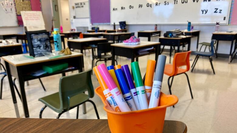 A bunch of markers stacked in a cup in an empty classroom.