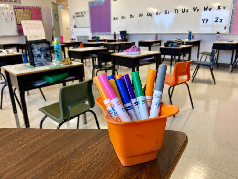 A bunch of markers stacked in a cup in an empty classroom.