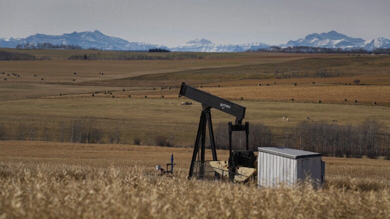 An oil well appears on a prairie field. Mountains are visible along horizon. 