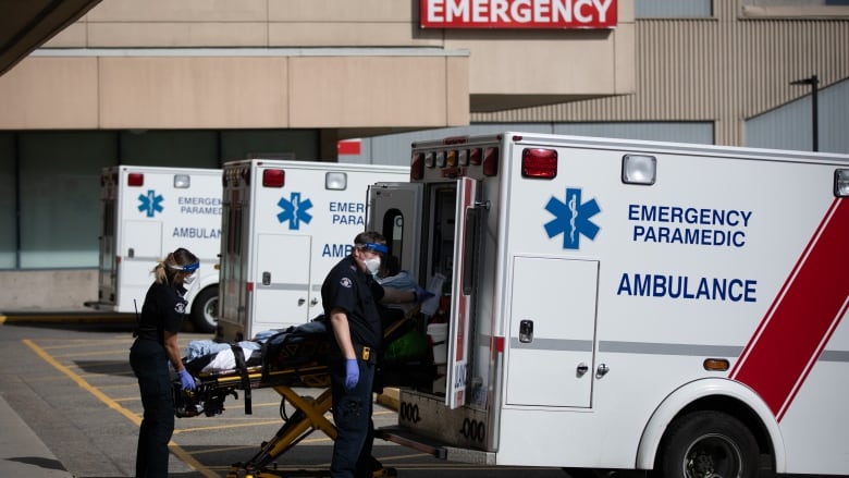 Two paramedics remove a person in a gurney from an ambulance in a parking lot.