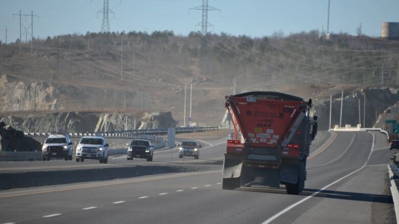 A big truck and some smaller trucks drive on a four-lane divided highway 