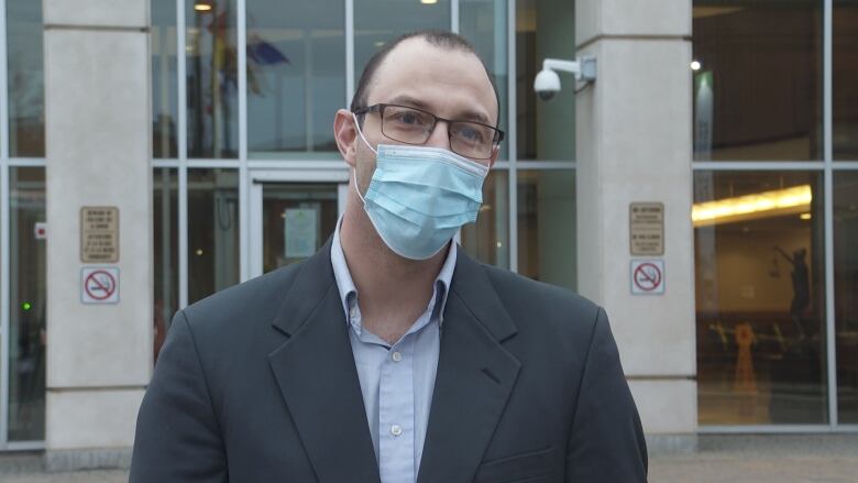 Man standing in front of a courthouse wearing a blue face mask. 