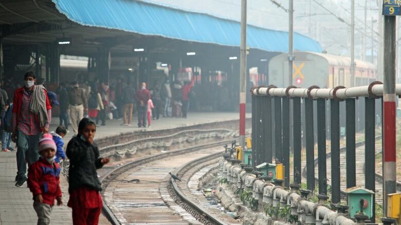 Two small children stand on a platform next to railway tracks.