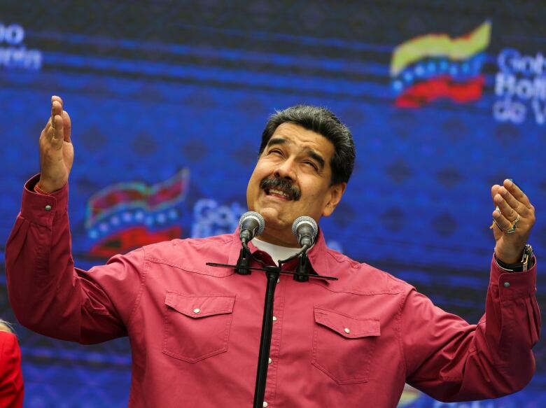 Maduro stands with his hands raised in a red shirt in front of a microphone. 