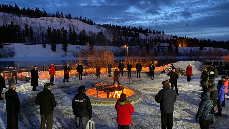 A group of people stand outside in a circle around a sacred fire.