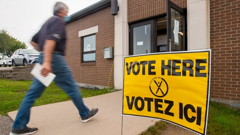 A man walking into a building with yellow Vote Here signs