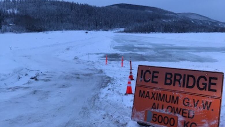 A sign saying 'ice bridge,' beside a frozen river in winter.