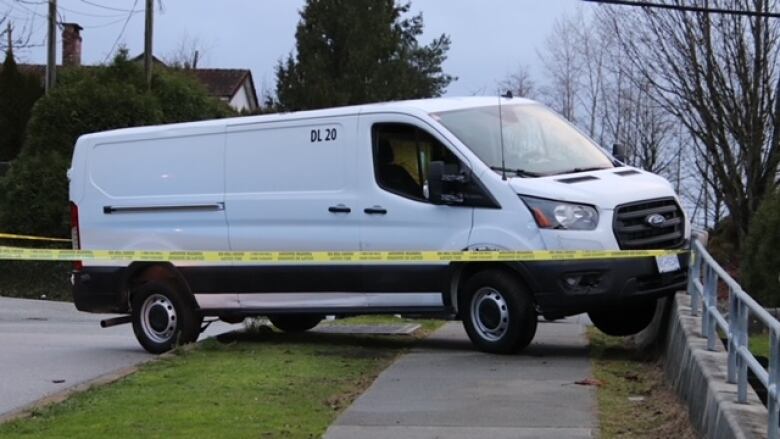 A white van stands on a sidewalk behind police caution tape.