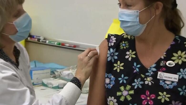 A nurse receives a COVID-19 vaccination from another nurse in a mask.