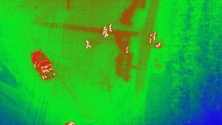 Thermal imaging from a drone shows people on the ground.