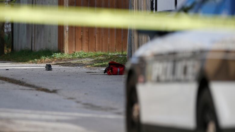 A shoe and a piece of clothing are seen on a backlane, while a police cruiser and yellow caution tape are located in front of it.