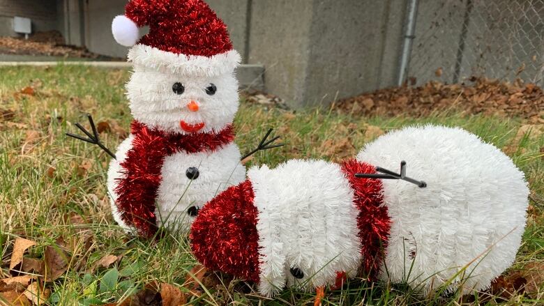 Two snowman lawn ornaments on a green lawn with one face down. 