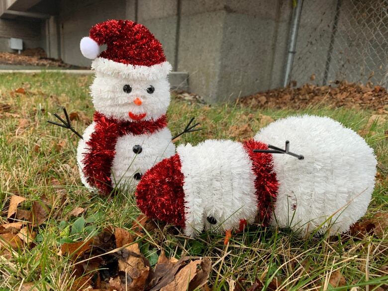 Two snowman lawn ornaments on a green lawn with one face down. 