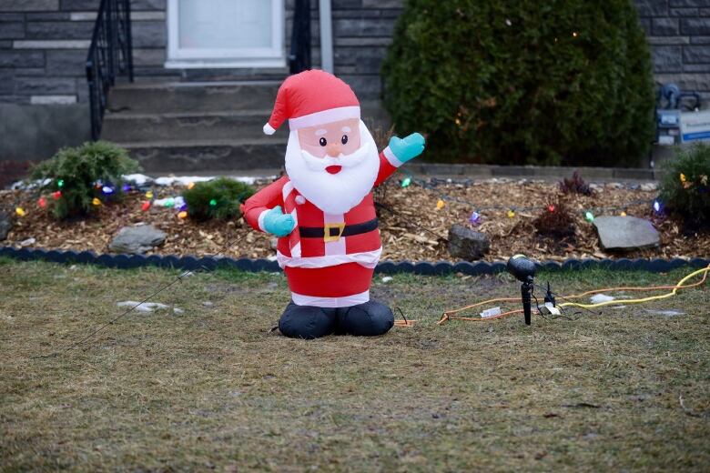 An inflatable santa on a green lawn with a teeny little bit of snow in the background. 