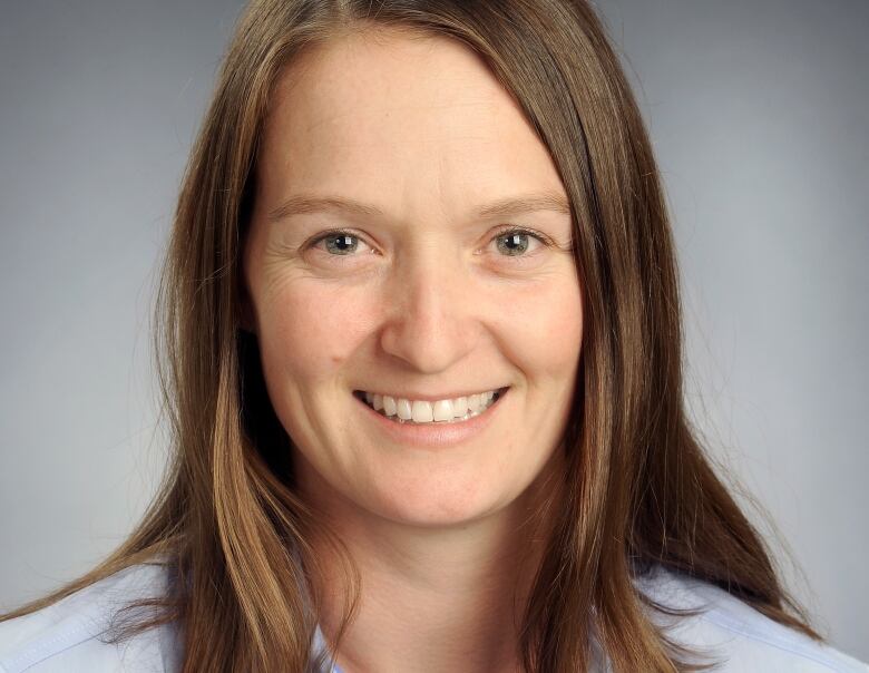 A close-up of a smiling woman in a blue button-up shirt.