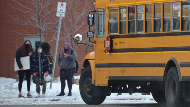 Three students stand outside a school bus.