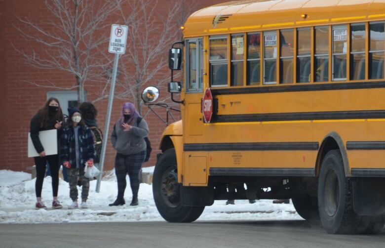 Three students stand outside a school bus.