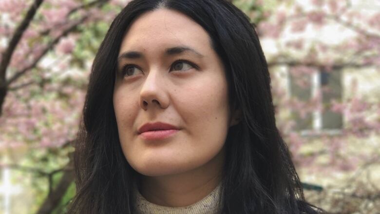 headshot of a British Canadian Taiwanese person with long black hair in front of a cherry blossom tree.