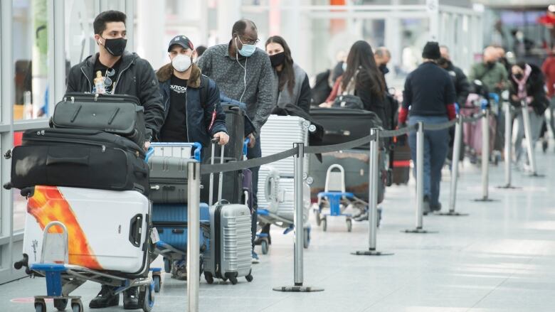 Masked people line up with luggage.