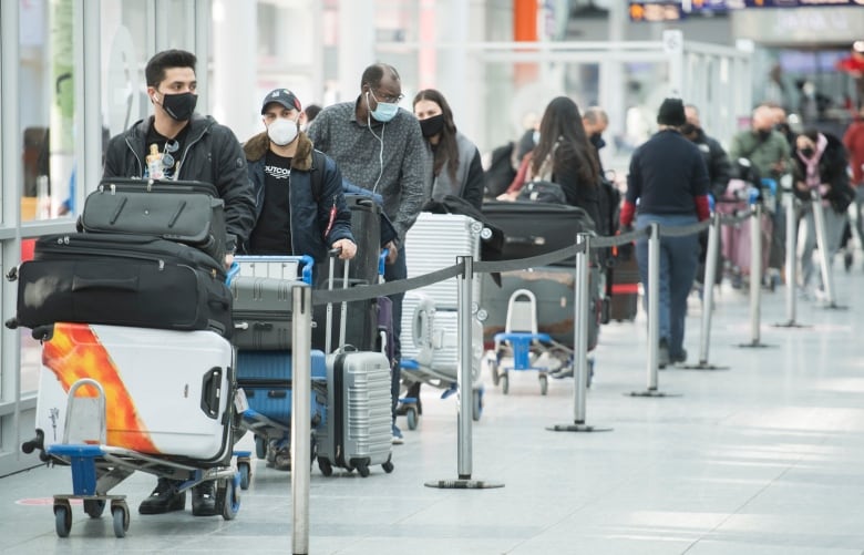 Masked people line up with luggage.