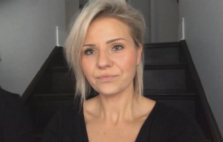 A woman looking directly into the camera sitting in front of steps. 