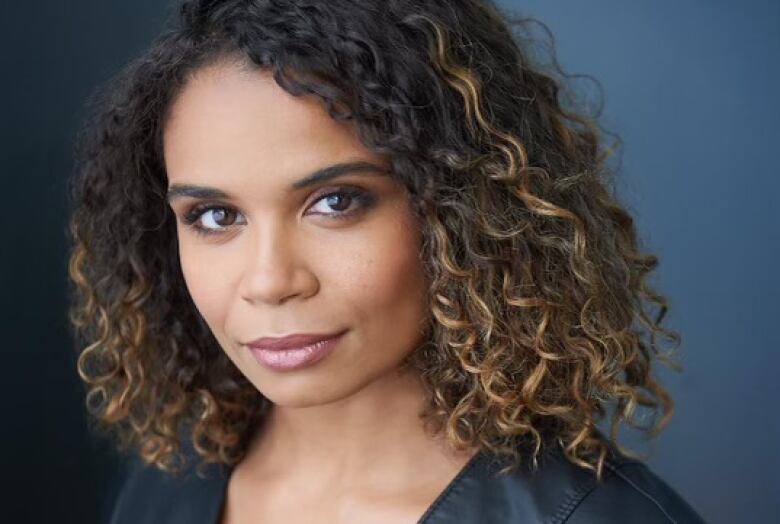 A black woman with curly hair poses for a portrait. 