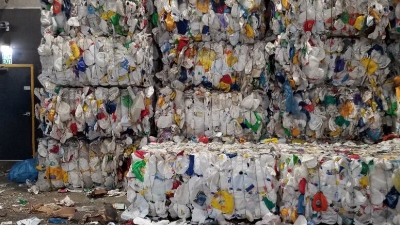 Large compacted bales of colourful plastic are stacked in a warehouse ready for shipping to a recycling facility.