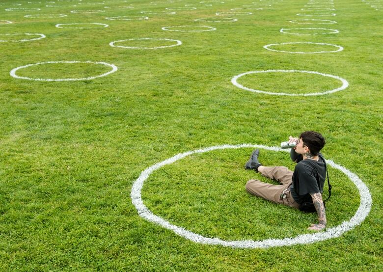 A man sips beer outdoors in a field of grass.