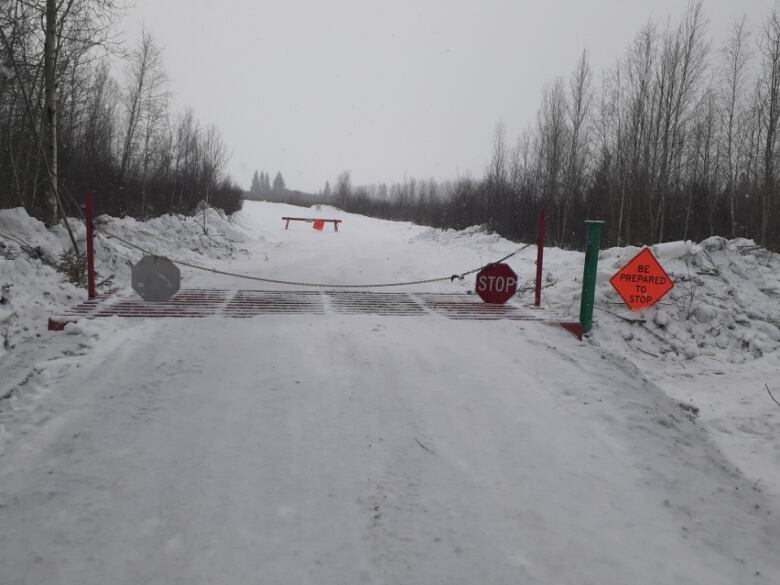 An icy road with a chain barrier and a stop sign blocking its path. 