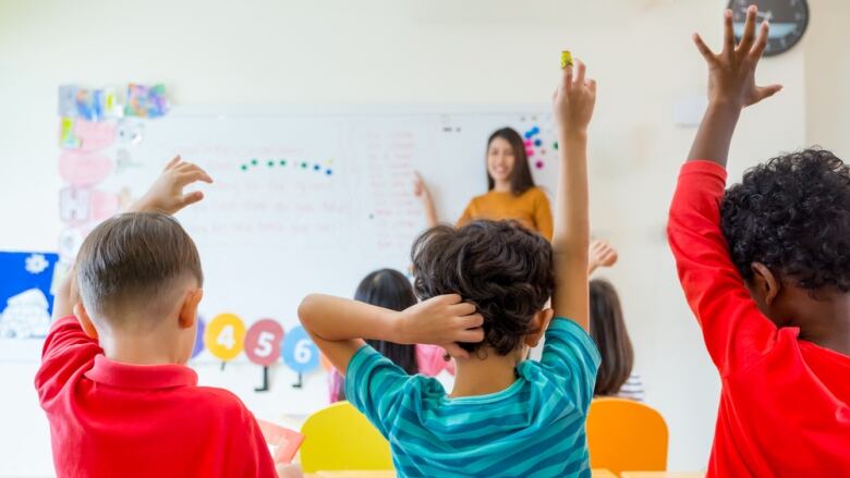 Groups of kids raise their hands in a classroom.