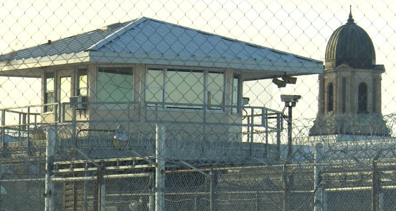 A prison is pictured behind a watchtower, and fencing is seen in front of both.