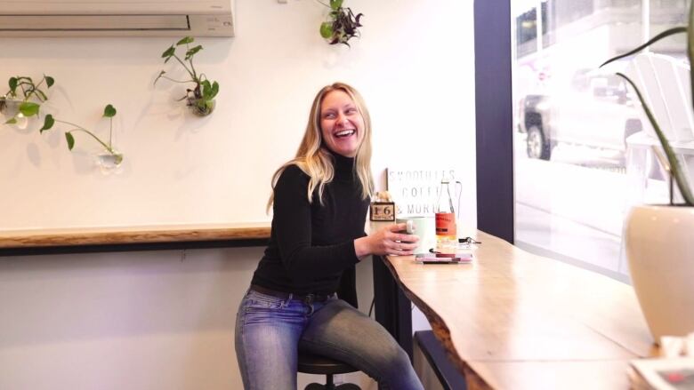 A smiling woman at a table with a cup of coffee.