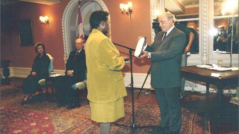 A woman stands in front of a man in a swearing-in ceremony.