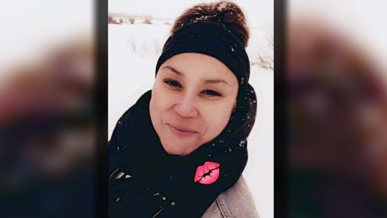 A woman smiles at the camera while wearing a black headband and black scarf. 